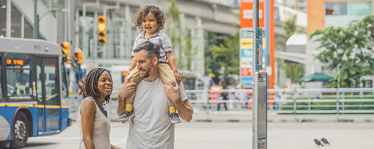 A family of three standing by a bus stop waiting for the bus
