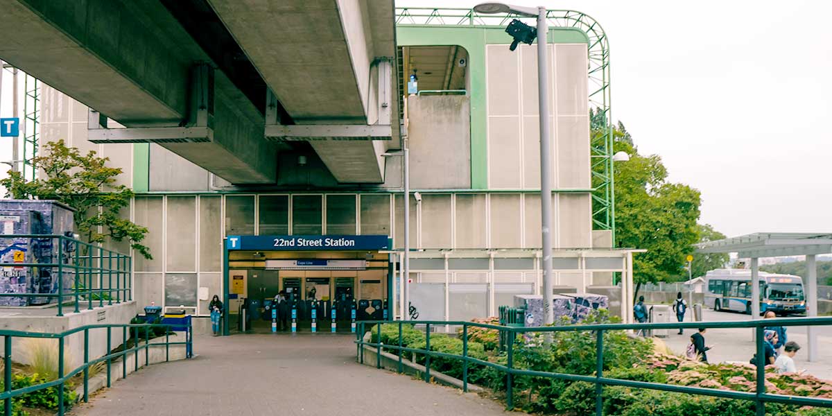 22nd Street Station entrance with fare gates, elevated track, transit signs, and nearby bus bay