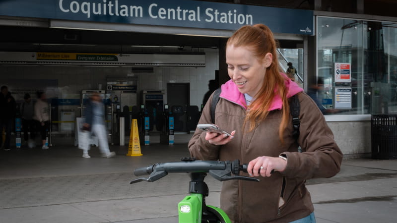 Customer looking at her phone with an e-bike in front of Coquitlam Central Station
