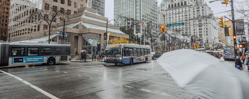 Two buses downtown during rainy weather with a grey umbrella in the foreground