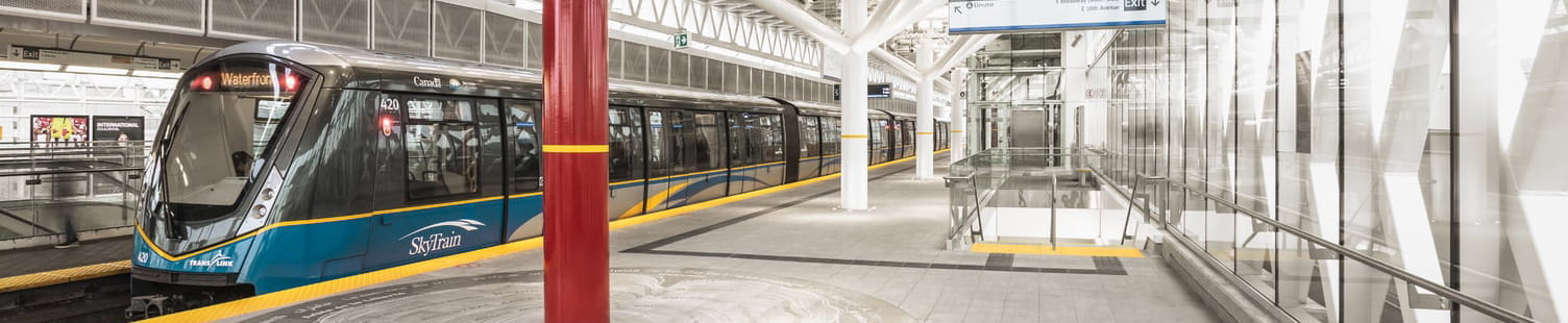 A SkyTrain docked at a station with a public art piece next to the train