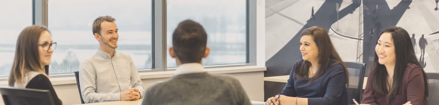 Five employees sitting around each other in a well-lit meeting room